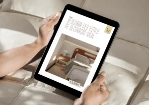 Pessoa segurando um ipad com a tela ligada na capa do Guia de Estilos de Decoração da Curva. Ao fundo, uma cama bege.
