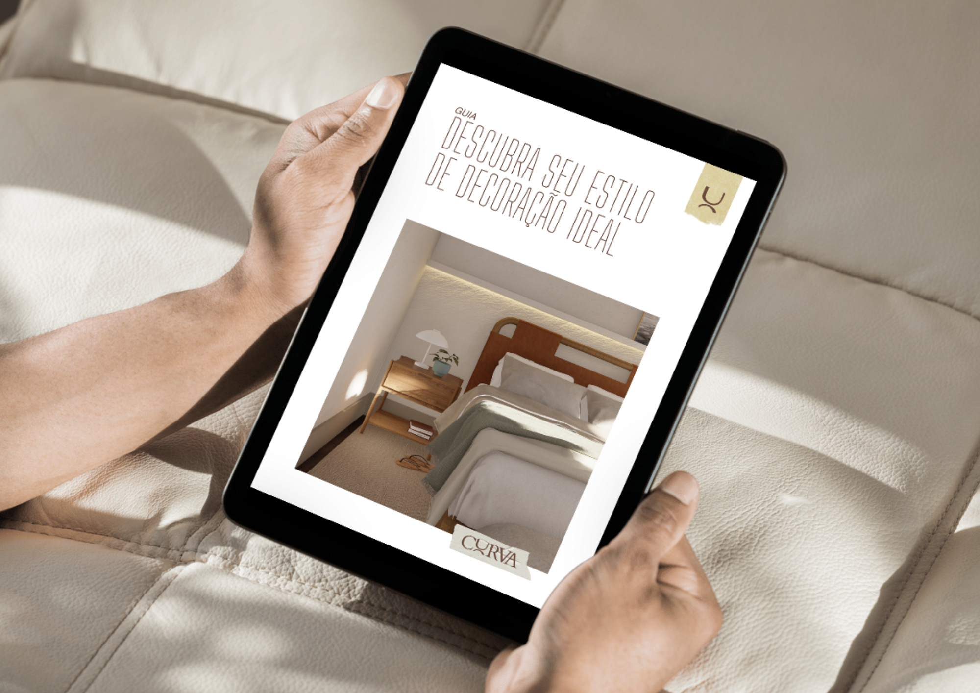 Pessoa segurando um ipad com a tela ligada na capa do Guia de Estilos de Decoração da Curva. Ao fundo, uma cama bege.